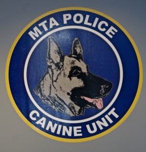 Logo of the mta police canine unit, featuring a stylized image of a german shepherd's head centered within a blue and yellow circular badge.
