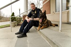 A police officer sitting on steps with his german shepherd police dog beside him, both looking relaxed.