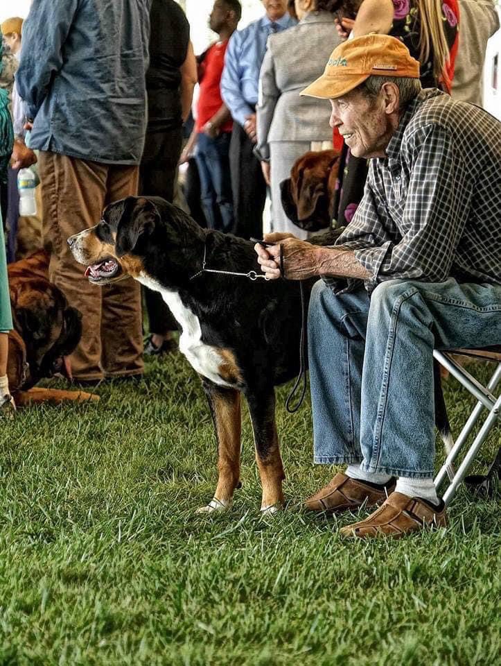 Old man with a tangerine cap petting a black Entlebucher Mountain Dog