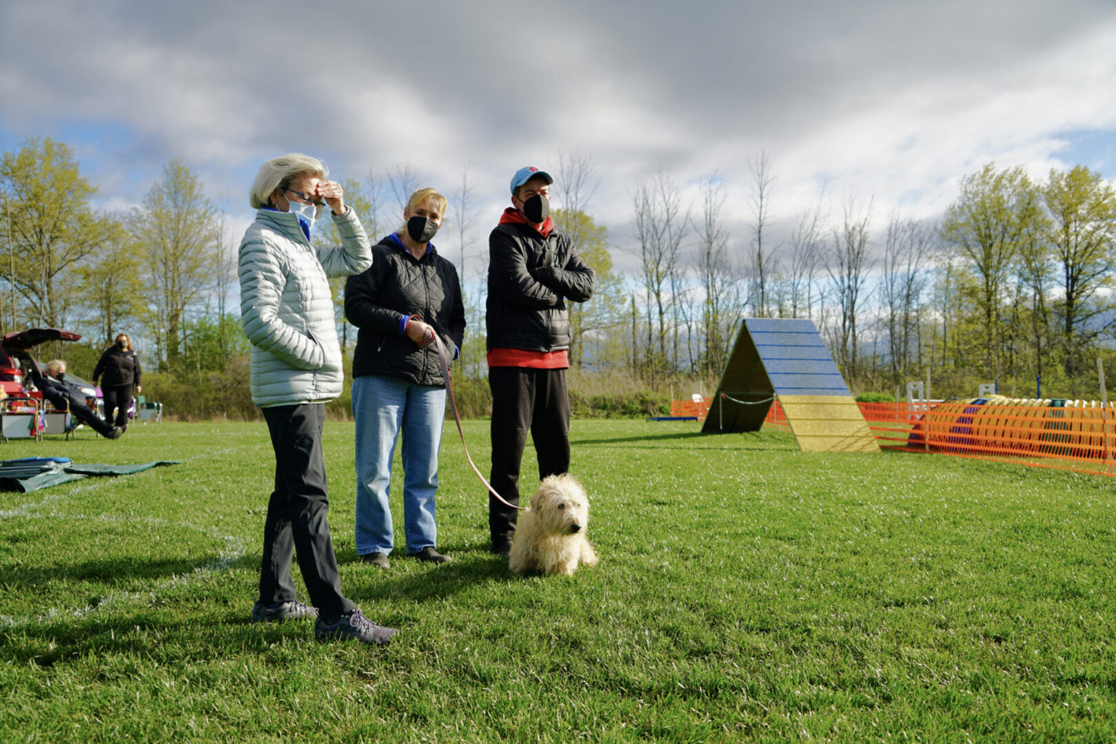 Three people in a dog training course with a cream-colored Terrier