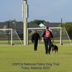 Two men and a patrol dog at the uspca national patrol dog trial in foley, alabama, 2023, walking across a soccer field.