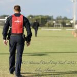 A man in a black uniform with a red "adlerhorst" vest walks across a grassy field at the uspca national patrol dog trial 2023 in foley, alabama.