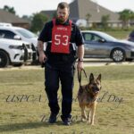 A police officer with a badge numbered 53 and a dog on a leash at a uspca national patrol dog event in foley, alabama.